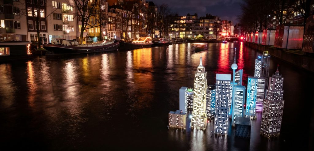 Instalación artística con forma de edificios iluminados proyectados sobre el canal durante el Amsterdam Light Festival.
