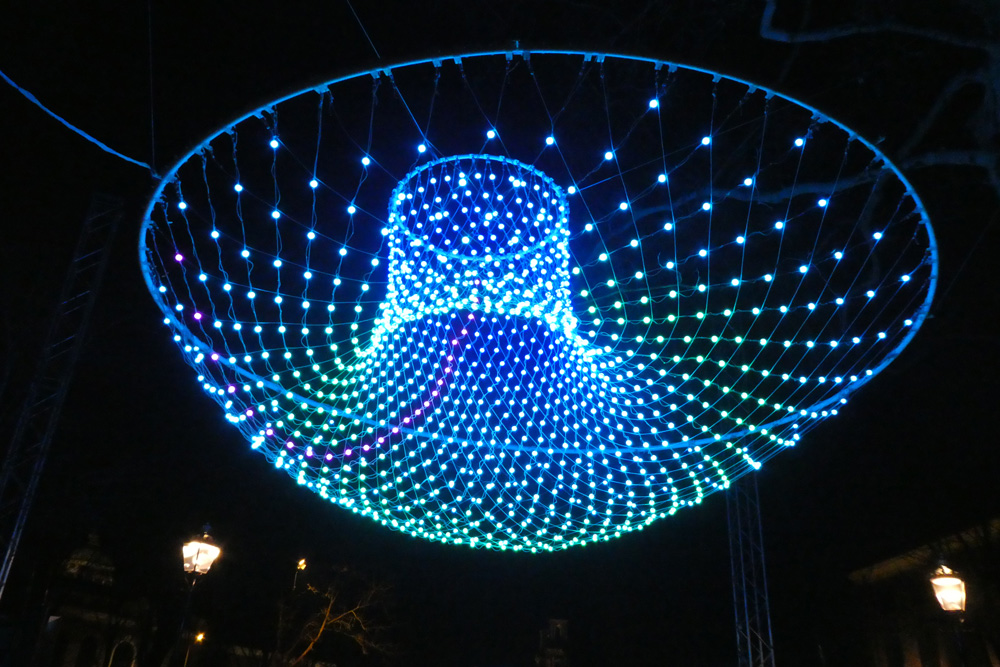Instalación de luces azules con formas flotantes suspendidas sobre el canal durante el Amsterdam Light Festival.