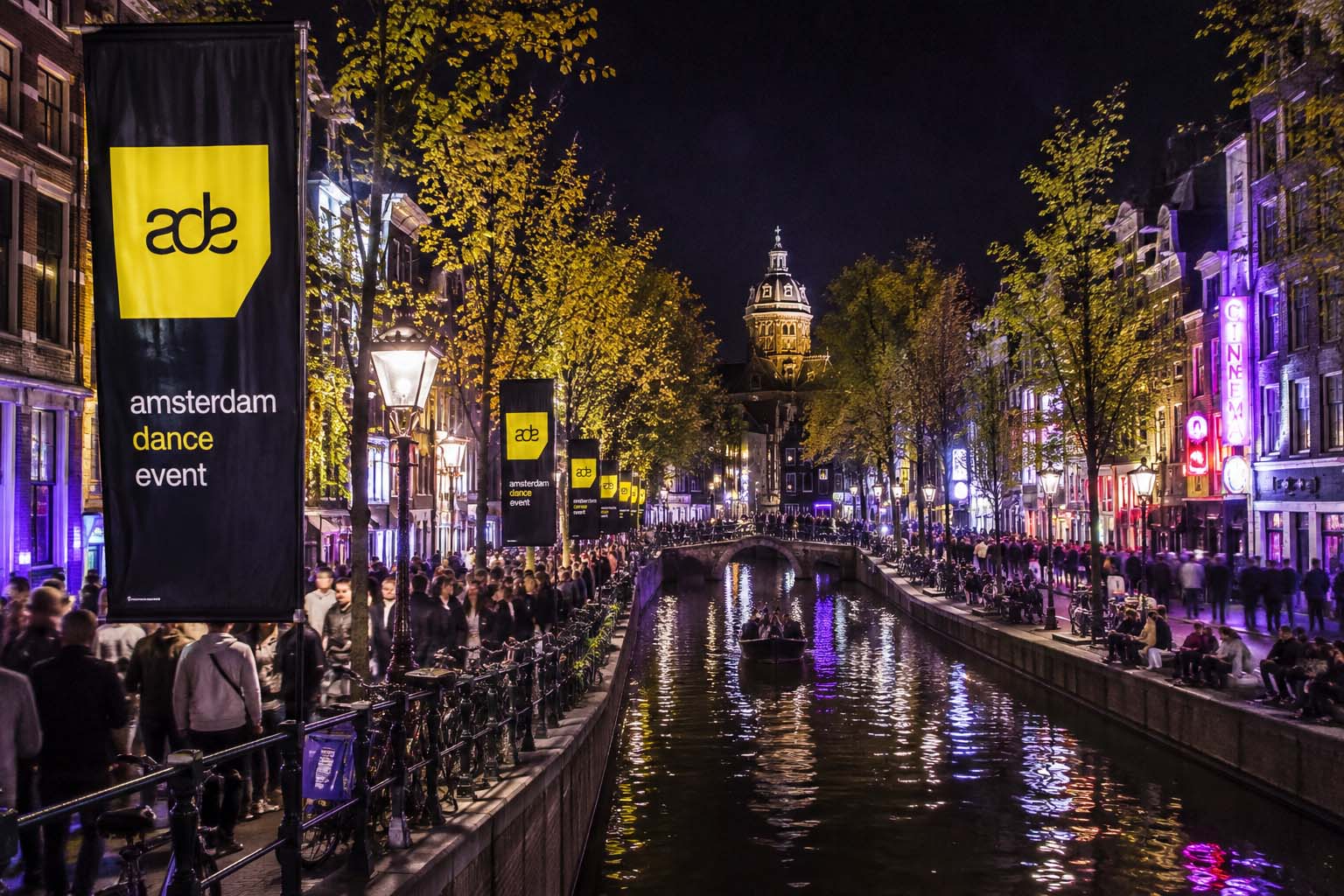 Canal de Ámsterdam de noche durante el Amsterdam Dance Event, con publicidad de ADE junto al agua y gente recorriendo las calles.