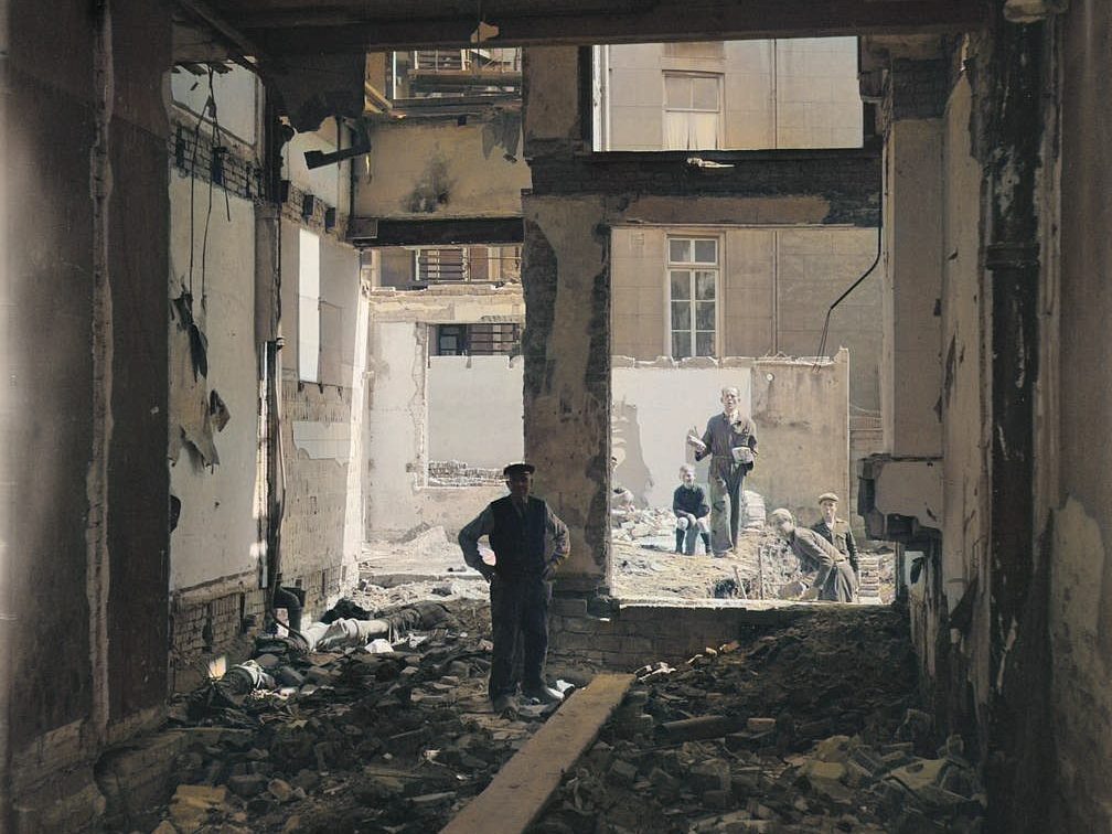Anciano dentro de una vivienda dañada tras el segundo bombardeo en Ámsterdam, con niños y vecinos observando los escombros desde la calle