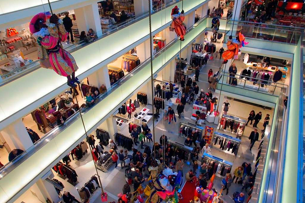Interior del centro comercial De Bijenkorf en Ámsterdam con luces y adornos navideños.