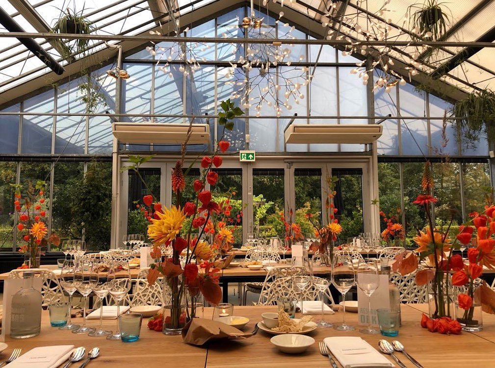 Interior del invernadero del restaurante De Kas en Ámsterdam con mesas preparadas para la cena.
