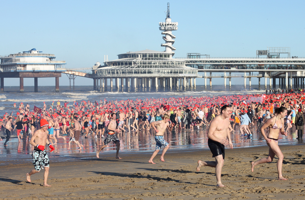 Participantes del Nieuwjaarsduik saliendo del mar en Scheveningen el 1 de enero con gorros naranjas.