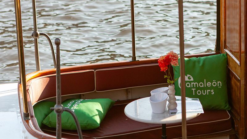 Barco de Camaleon Tours navegando por los canales de Ámsterdam con decoración corporativa.