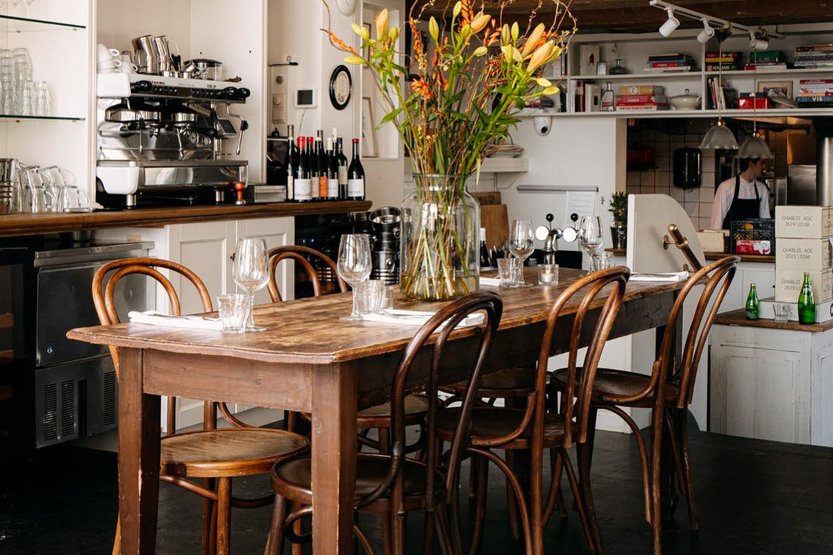 Mesa preparada en el restaurante Tannay con botellas de vino y personal al fondo junto a la barra.