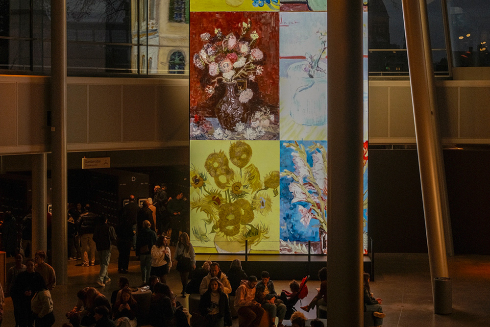 Interior del Museo Van Gogh con pantalla vertical que muestra varias pinturas de flores en jarrones de Van Gogh.