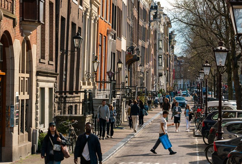Calle de Ámsterdam por la mañana con personas paseando y ambiente relajado.