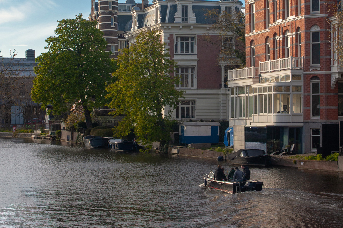 Cinco jóvenes disfrutan de un paseo en barco por los canales de Ámsterdam, rodeados de arquitectura histórica y reflejos en el agua.