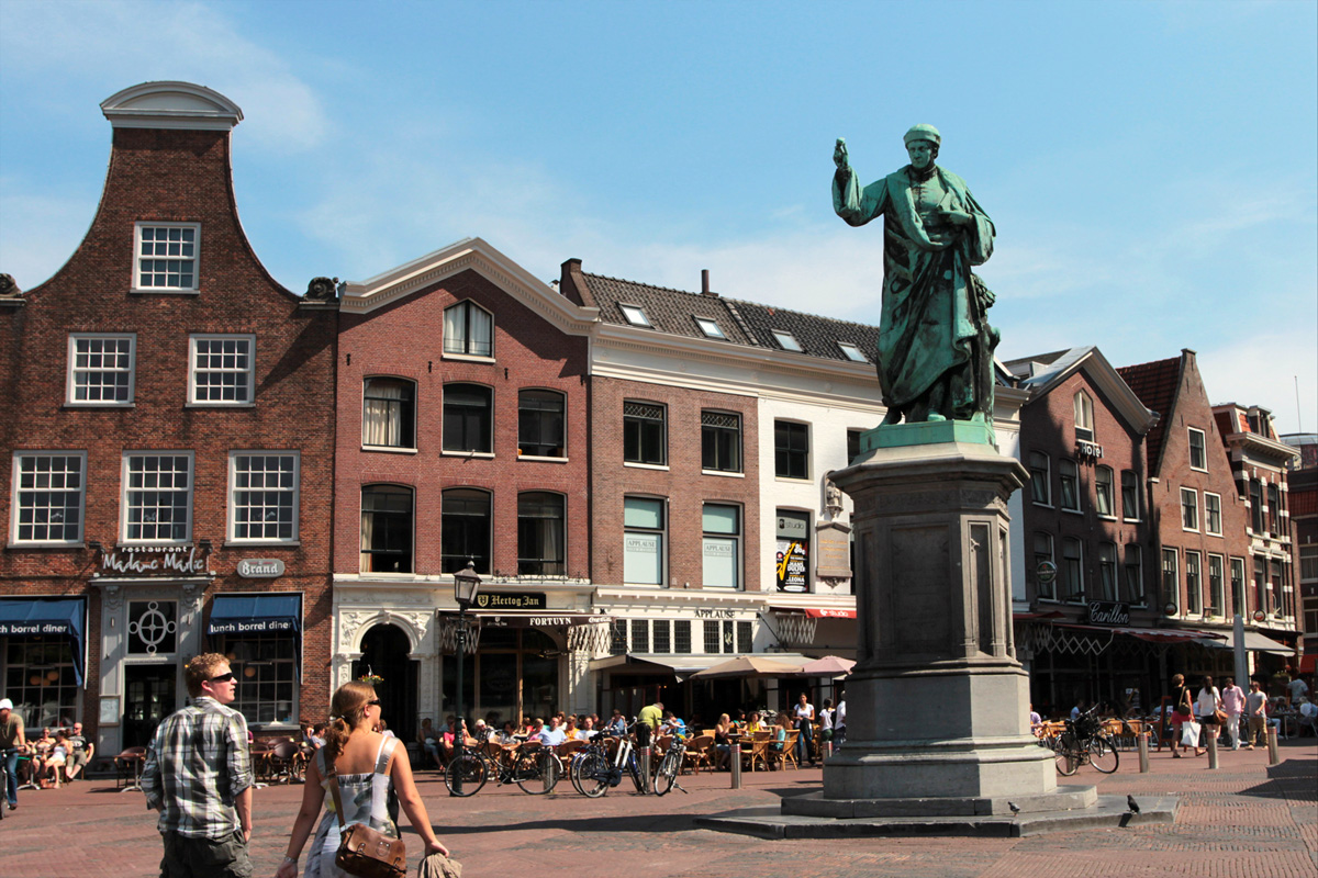Grote Markt en Haarlem con el monumento a Laurens Coster, una pareja paseando y personas disfrutando del sol en las terrazas.