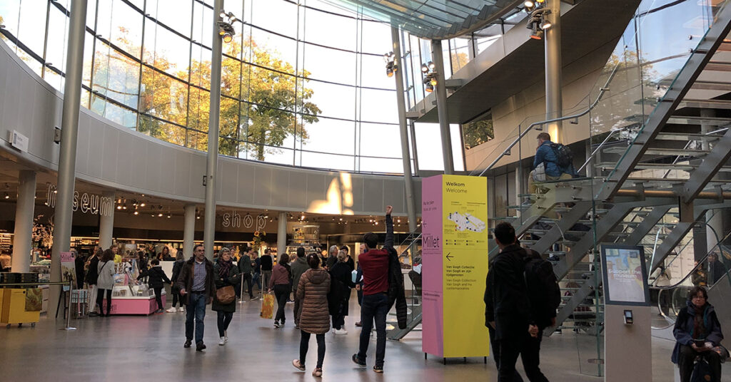 Vestíbulo del Museo Van Gogh en Ámsterdam, con visitantes abrigados paseando entre cristaleras modernas, en un día de invierno