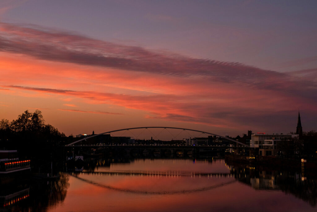 Puente de Maastricht al atardecer, con cielo dorado y reflejos sobre el río Mosa.