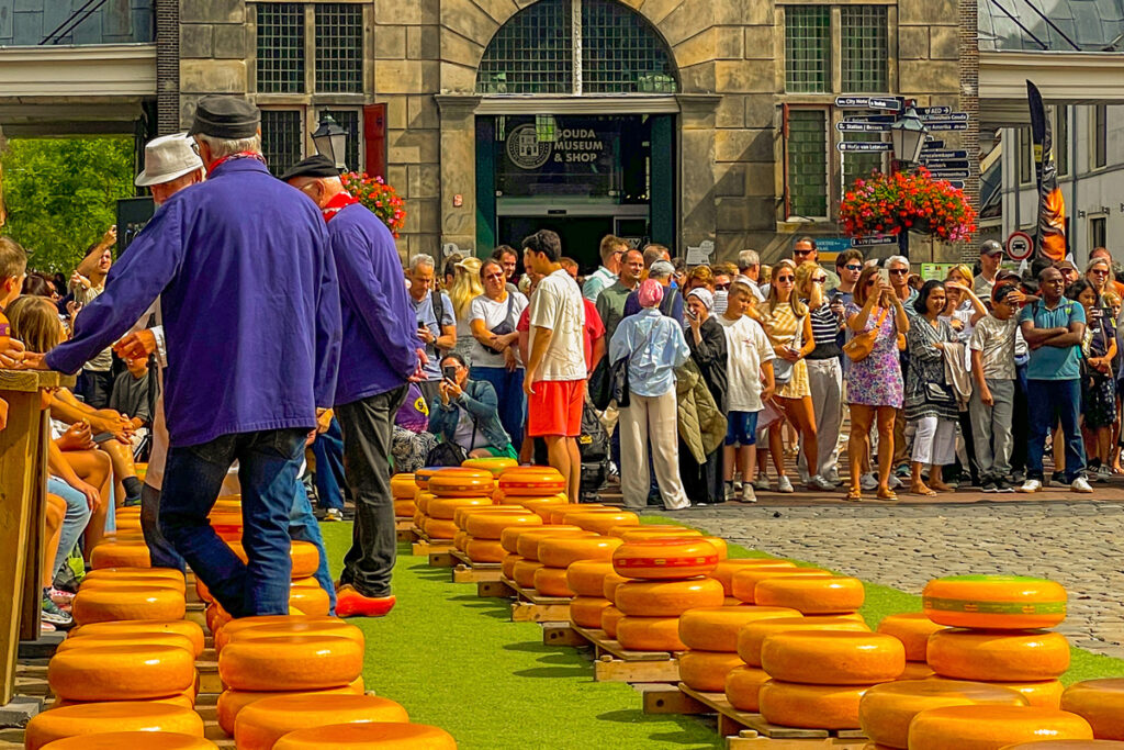 Escena del Goudse Kaasmarkt en la Markt de Gouda, con queseros tradicionales, ruedas de queso y visitantes observando la actividad.