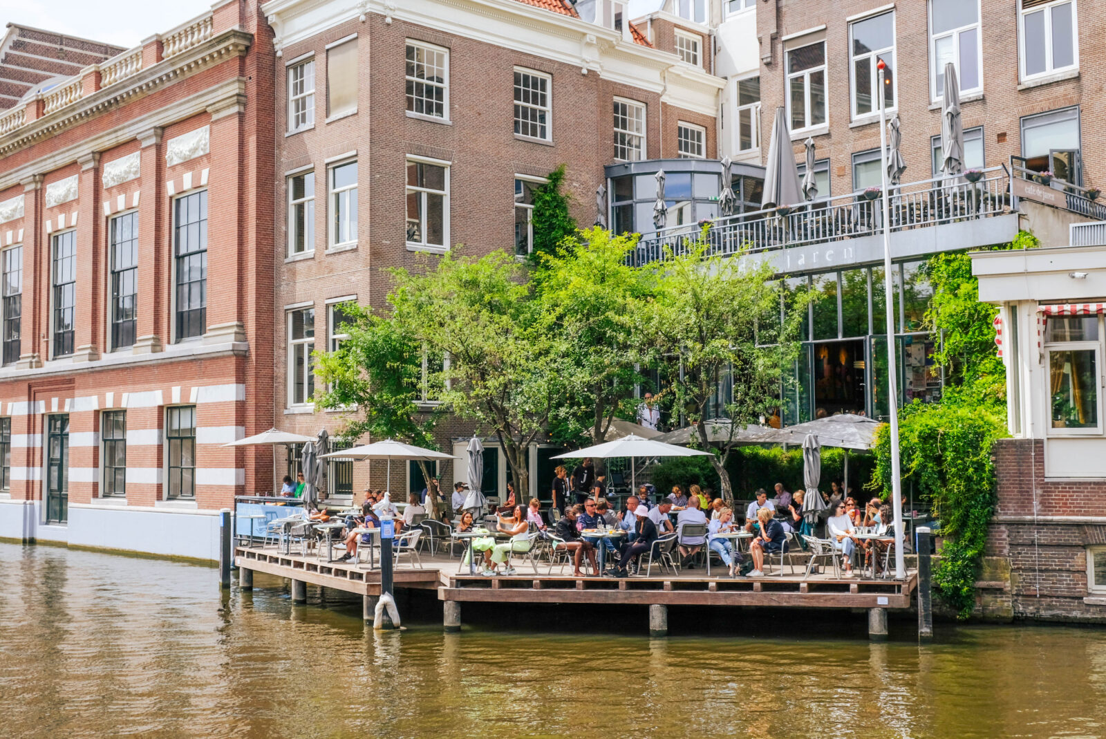 Vista desde el canal de la terraza soleada del Café de Jaren en Ámsterdam, con mesas al aire libre junto al agua.