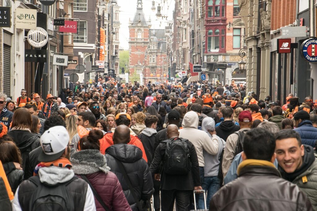 Calle de Ámsterdam con peatones celebrando el Día del Rey, muchos vestidos de naranja y disfrutando del ambiente festivo.