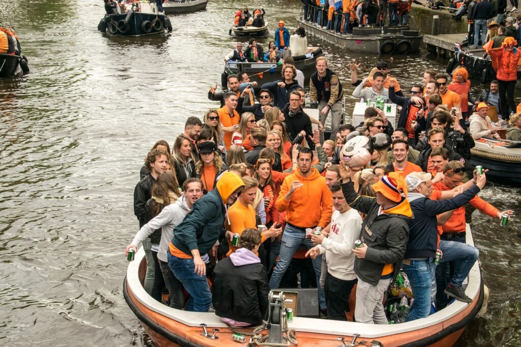 Jóvenes vestidos de naranja celebran el Día del Rey a bordo de un barco en los canales de Ámsterdam, con música y ambiente festivo.