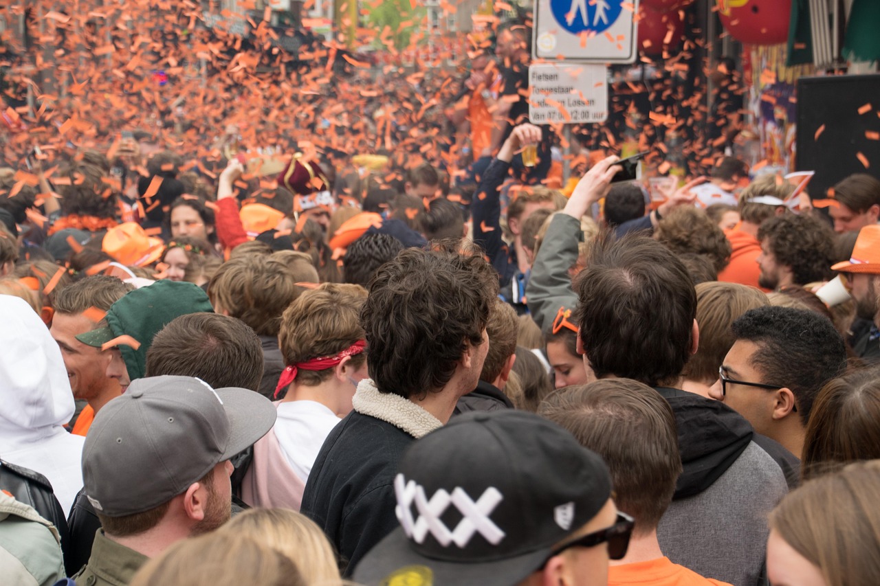 Multitud celebrando el Día del Rey en Ámsterdam, con confeti naranja en el aire y calles llenas de personas vestidas de naranja.