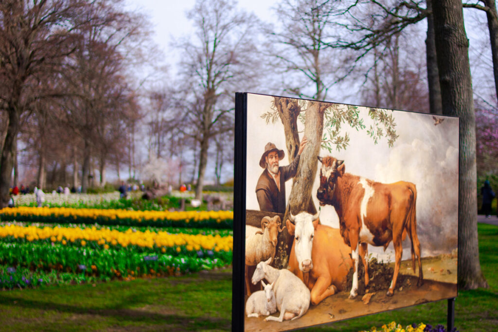 Pintura exhibida en el parque Keukenhof con campos de flores al fondo; arte visual integrado en el entorno floral del jardín.