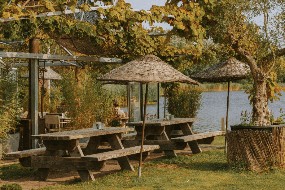 Zona verde al aire libre en el restaurante Como & Co, en Noordwijkerhout, con vistas al lago Oosterduinse Meer y vegetación primaveral.