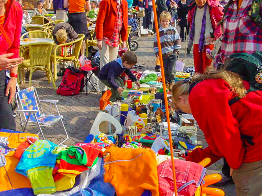 Niños y familias recorriendo el Vrijmarkt en Ámsterdam durante el Día del Rey, con puestos callejeros y objetos a la venta.