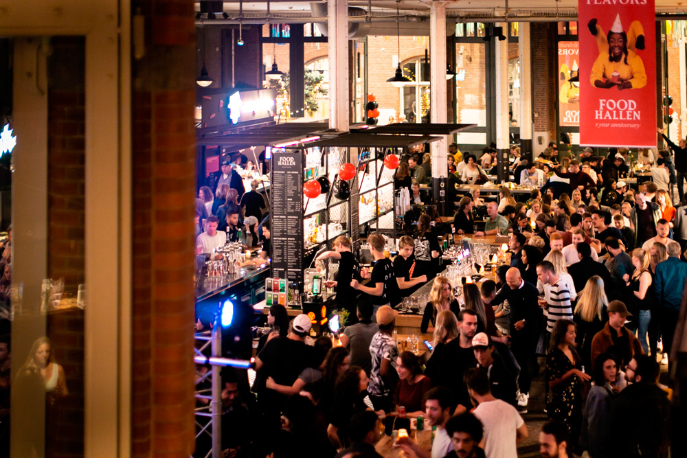 Vista desde arriba del mercado gastronómico Foodhallen en Ámsterdam, con numerosos puestos de comida y visitantes en mesas compartidas.