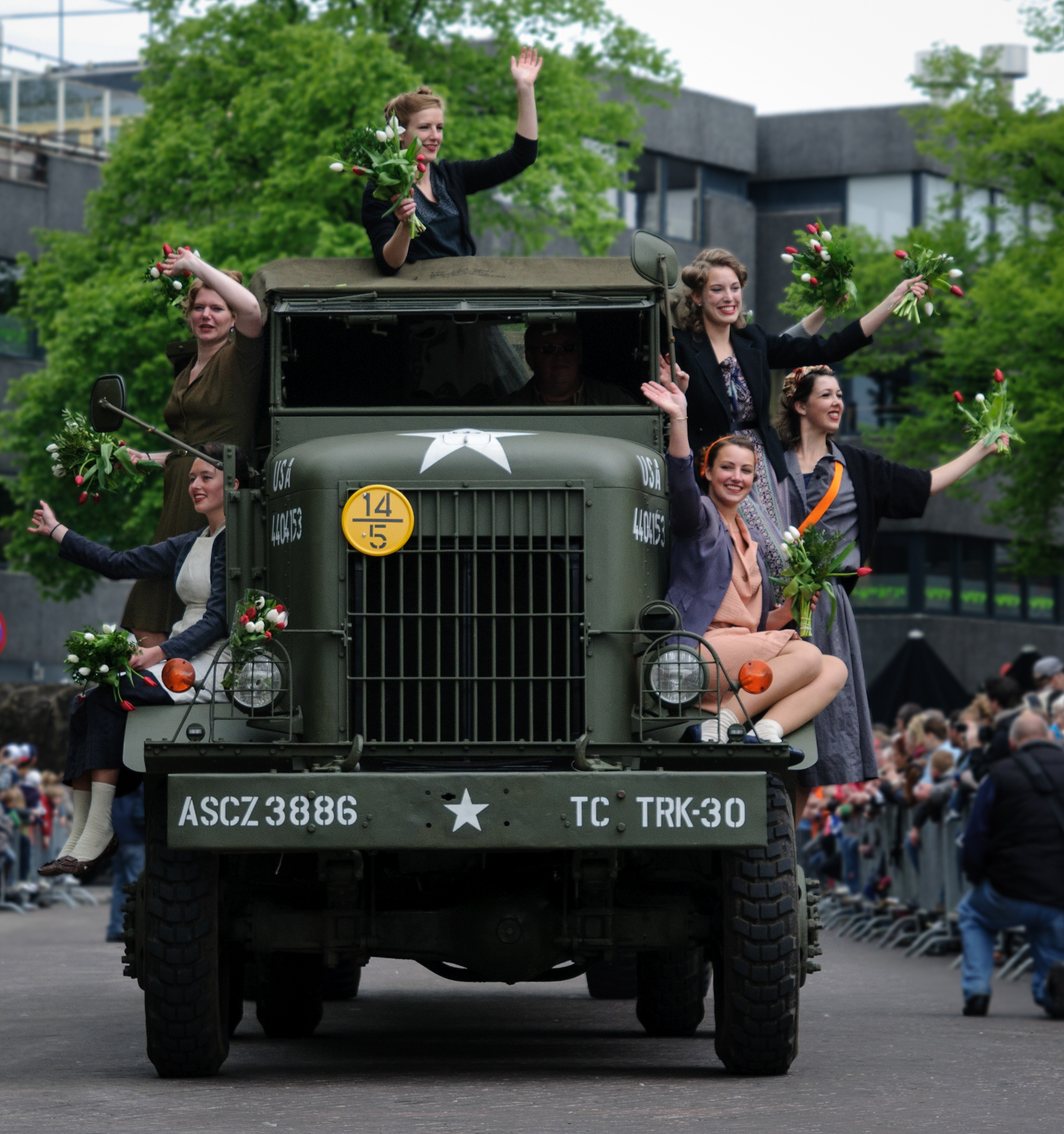 Camión militar histórico en un desfile del Día de la Liberación en los Países Bajos, con mujeres vestidas con ropa de época de los años 40.