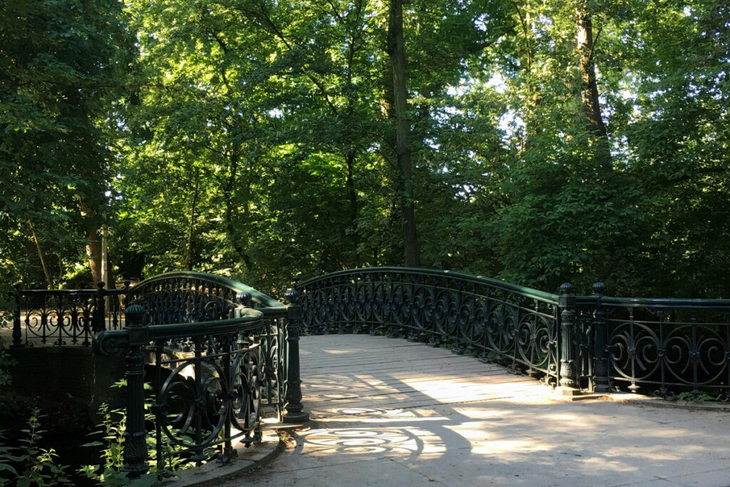 Zona arbolada del Vondelpark en Ámsterdam con un puente de hierro sobre un canal, rodeado de vegetación primaveral.