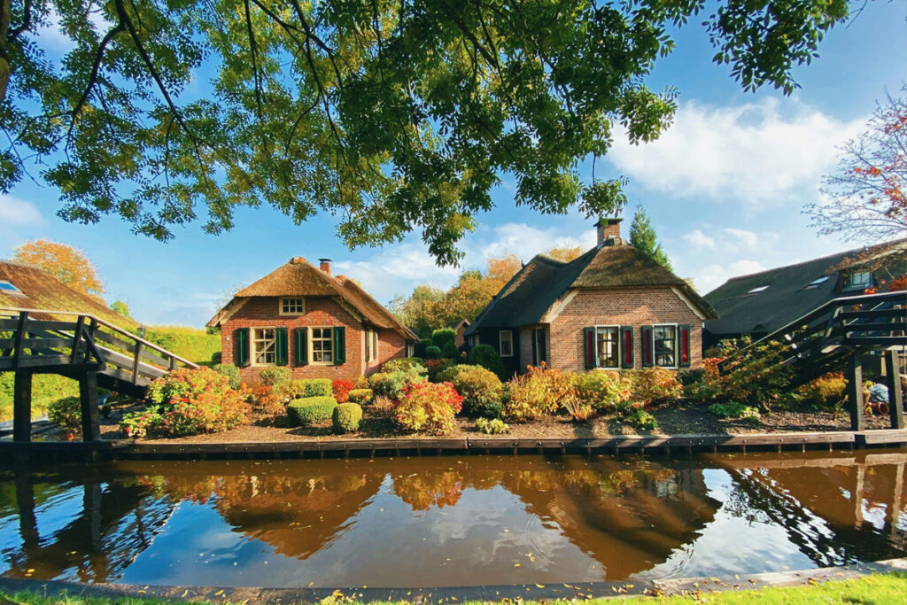 Casas tradicionales con techo de paja junto a un canal en Giethoorn, con jardines cuidados y agua tranquila en verano.