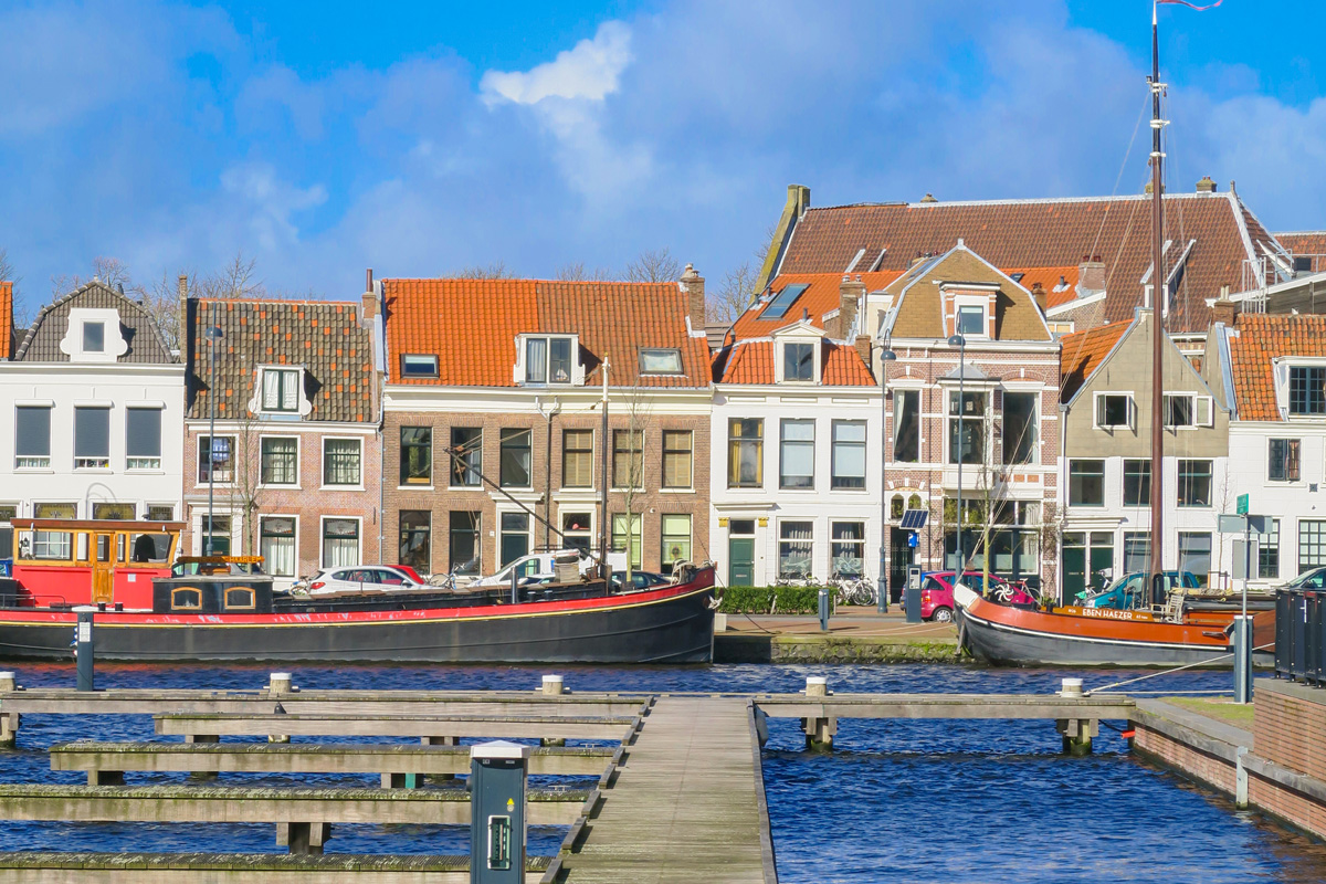 Muelle con barcos en un canal y casas tradicionales neerlandesas al fondo en una ciudad como Haarlem.