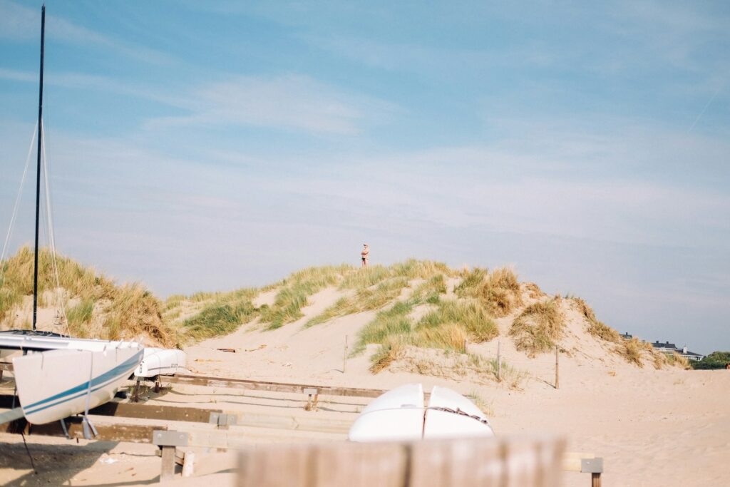Barcos sobre la arena en la playa de IJmuiden con dunas y una persona al fondo en un entorno natural.
