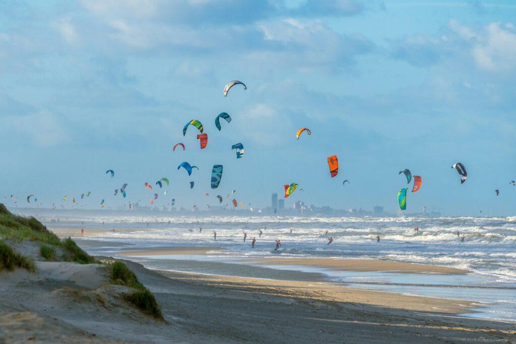 Playa de Noordwijk en verano con parapentes en el cielo, arena amplia y personas disfrutando junto al mar.