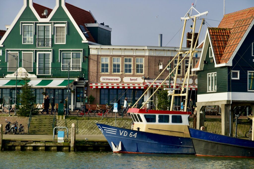 Muelle de Volendam con barcos atracados y casas tradicionales verdes junto al agua en un día de verano.
