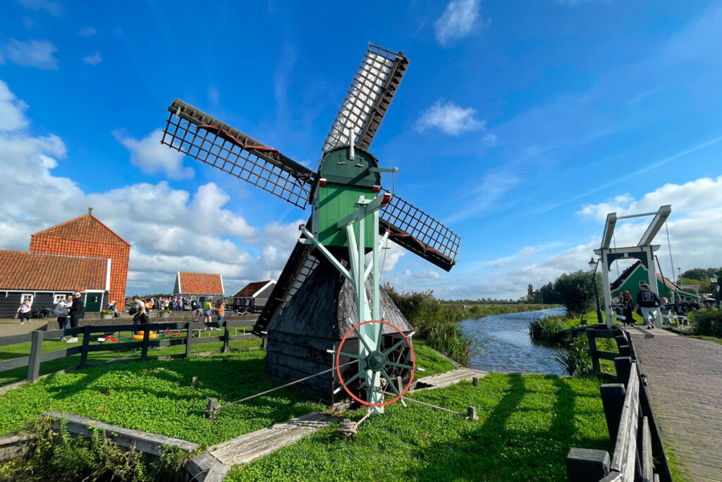 Molino de viento en Zaanse Schans con un puente blanco a la derecha y turistas visitando la zona.