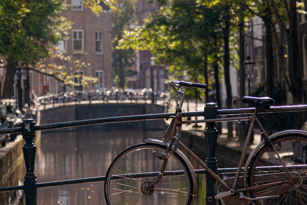 Bicicleta aparcada en un puente de canal en Ámsterdam en un día soleado, con el agua reflejando la luz del verano.