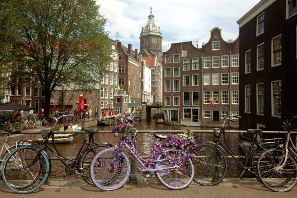 Varias bicicletas aparcadas en un puente de canal en Ámsterdam, una de ellas decorada en color violeta con flores.