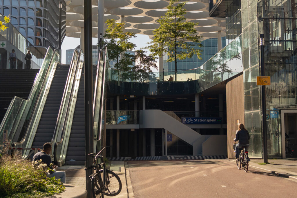 Mujer en bicicleta entrando a un aparcamiento de bicicletas en Utrecht, con infraestructura ciclista urbana.