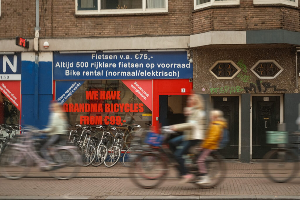 Carril bici en un barrio de Ámsterdam con ciclistas yendo al trabajo y al colegio, con una tienda de bicicletas al fondo.