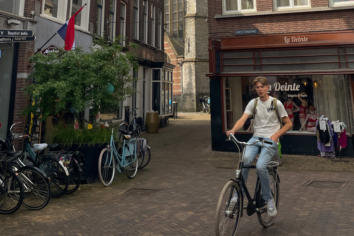 Hombre paseando en bicicleta por una calle del centro de Gouda entre edificios históricos neerlandeses.