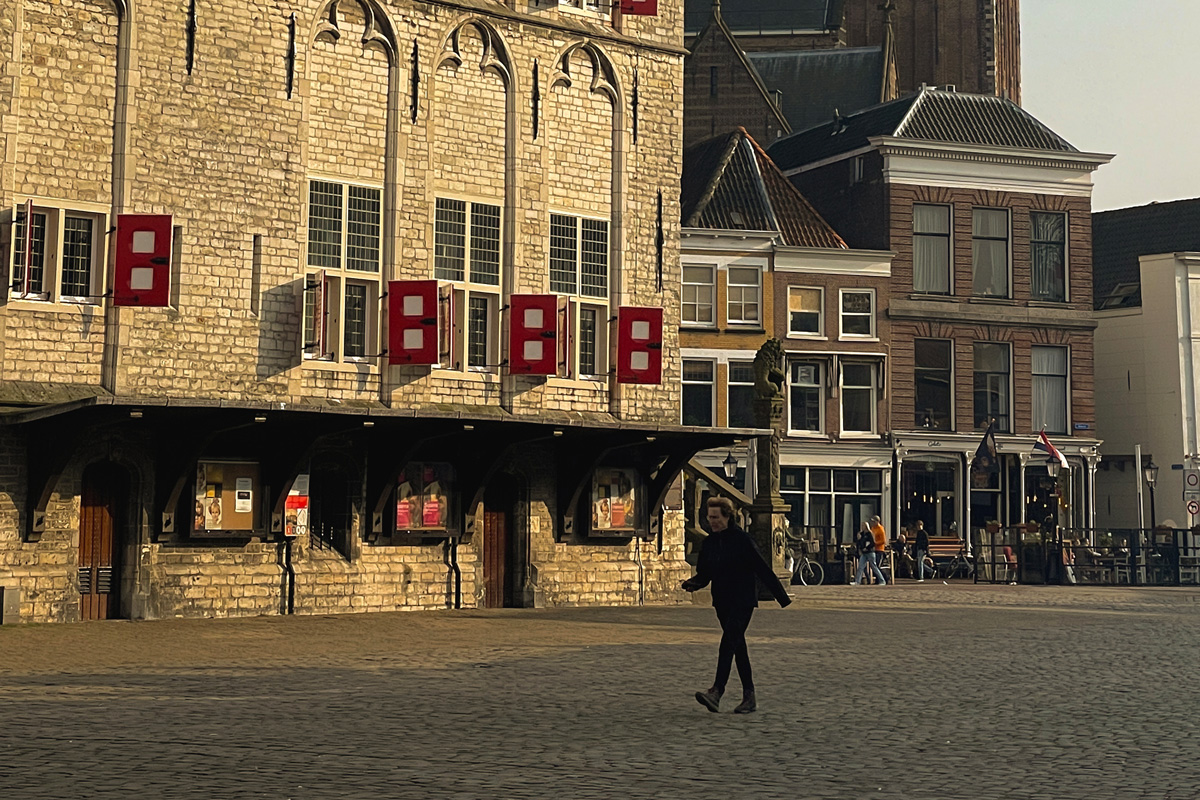 Mujer caminando por la plaza Markt de Gouda al amanecer, con el ayuntamiento histórico al fondo.