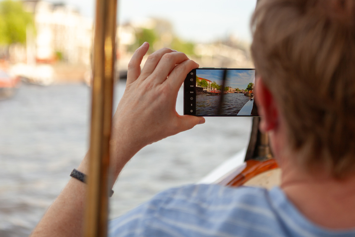 Joven fotografiando los canales de Ámsterdam con su teléfono móvil en un día soleado.