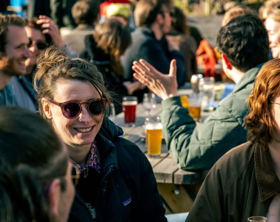 Personas disfrutando de cervezas artesanales en la terraza de De Kromme Haring durante un día soleado en Utrecht.