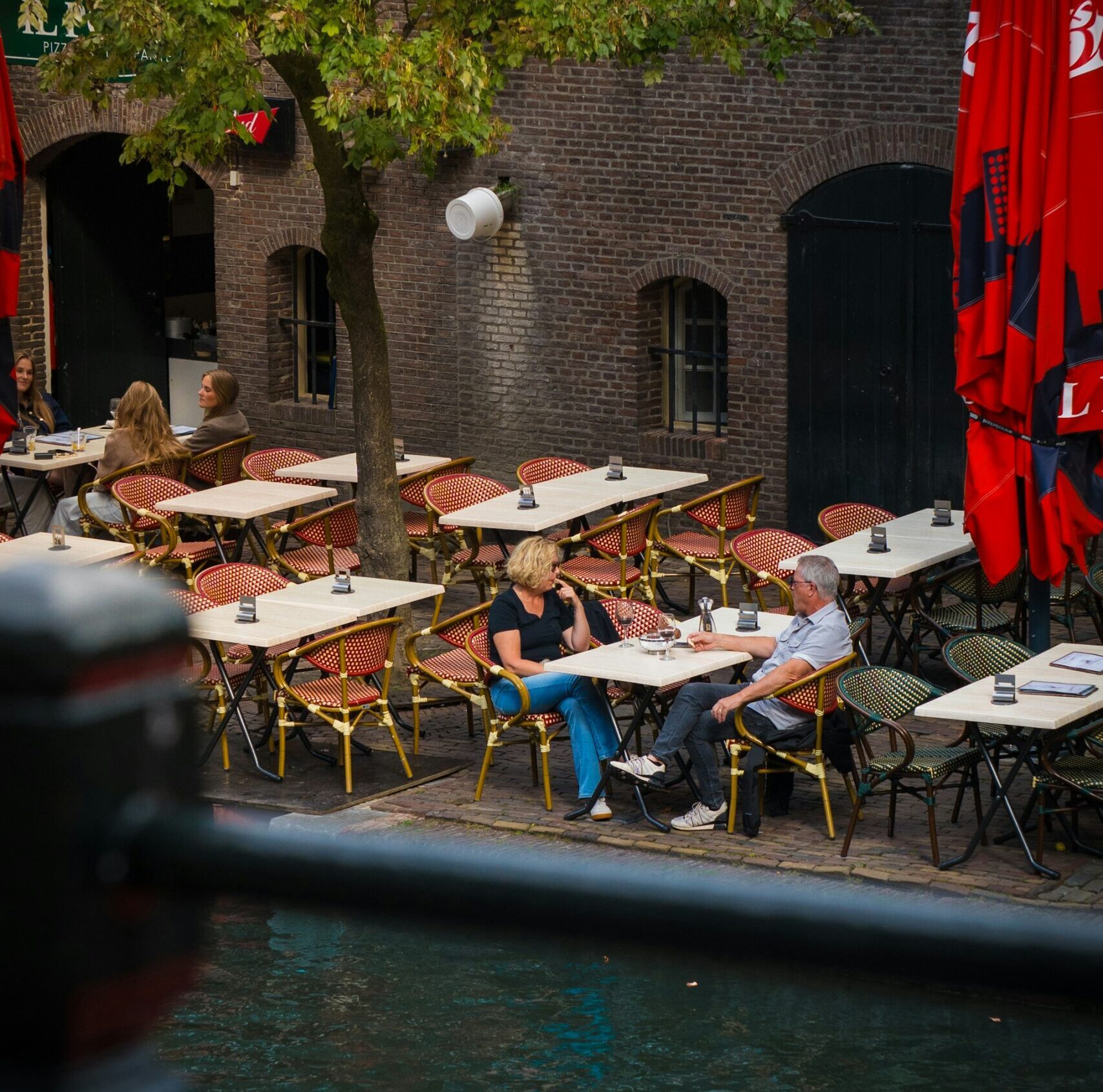 Personas disfrutando de una terraza junto al canal Oudegracht en Utrecht en un día soleado.