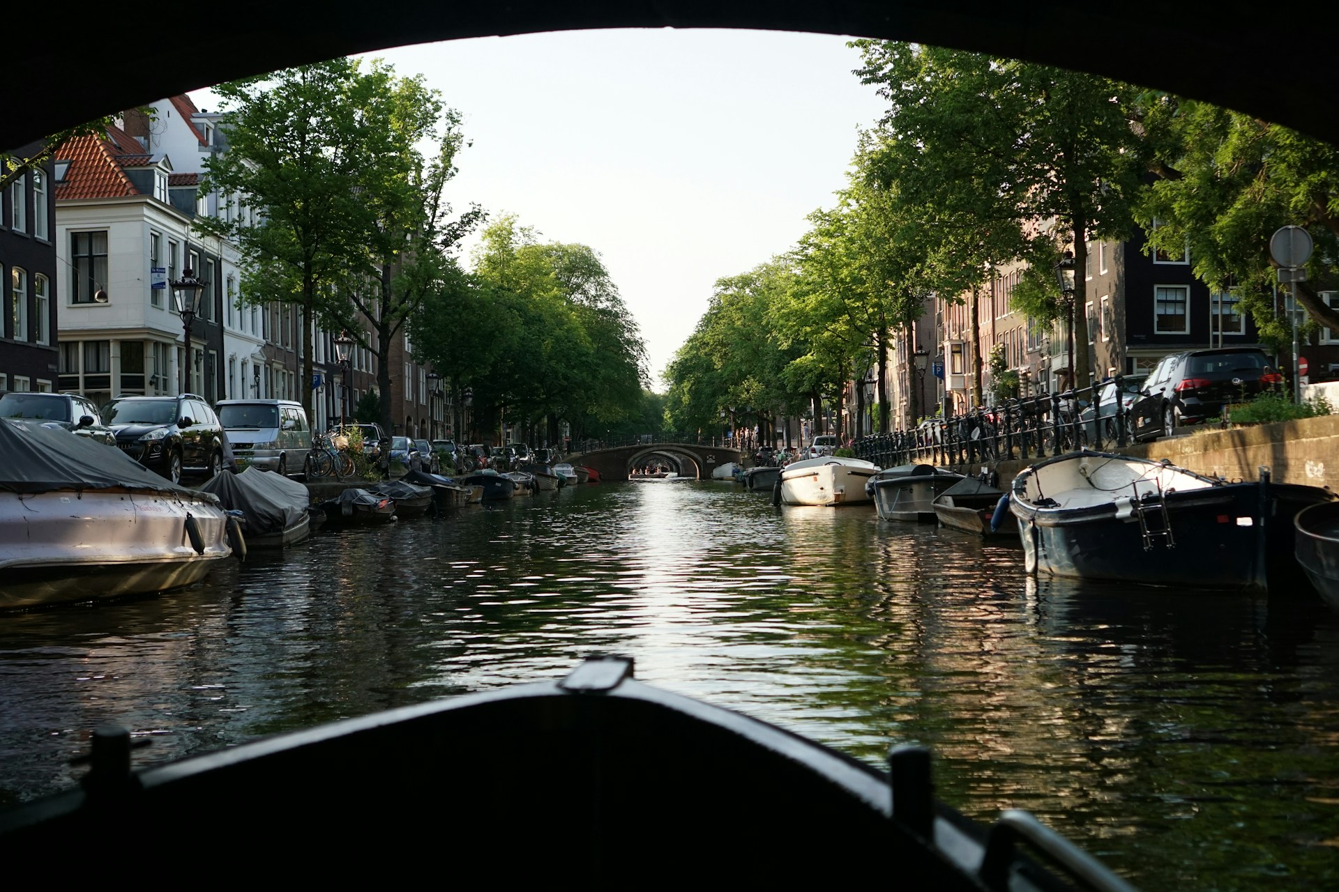 Pequeña barca navegando por un canal de Ámsterdam mientras pasa bajo un puente en una zona tranquila de la ciudad.