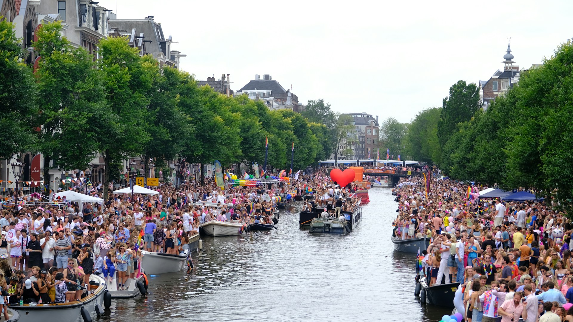 Canal de Ámsterdam lleno de espectadores observando embarcaciones decoradas durante la Canal Parade del Orgullo.