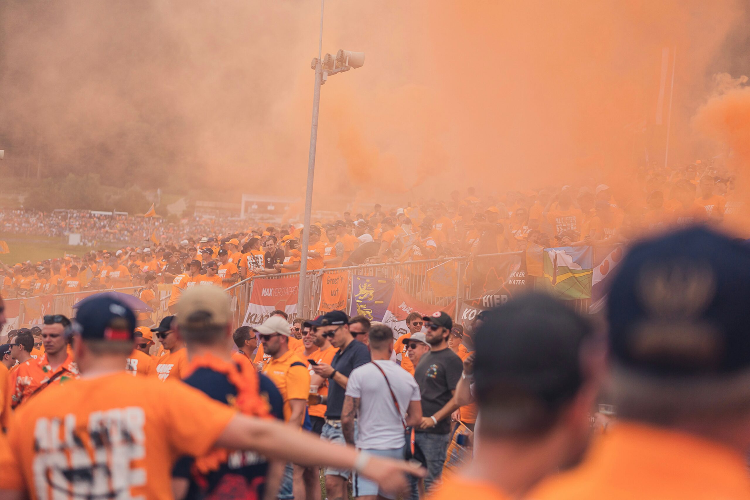 Aficionados neerlandeses rodeados de humo naranja durante un evento deportivo en los Países Bajos.