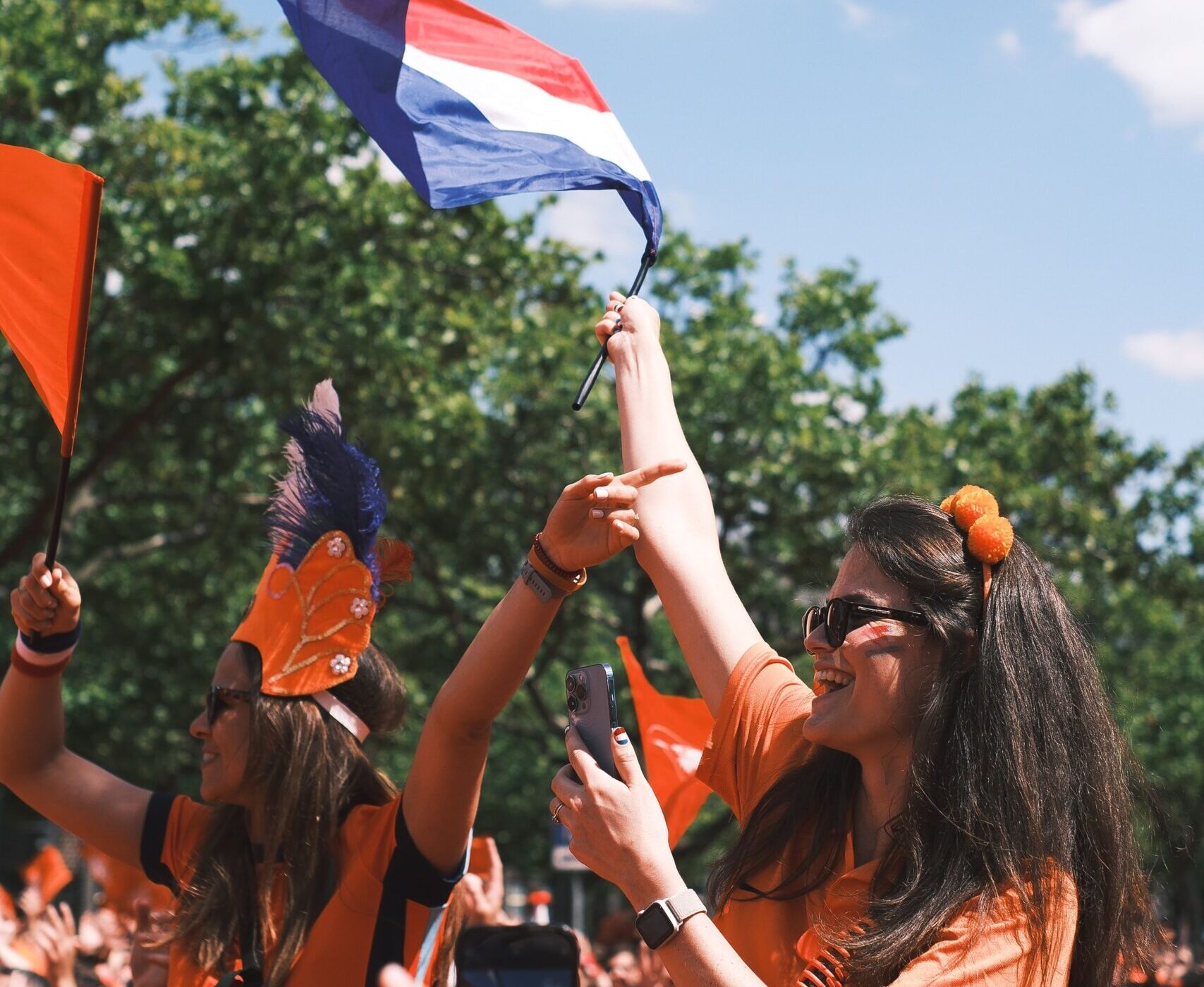 Jovenes vestida de naranja sosteniendo una bandera de los Países Bajos durante una celebración nacional.