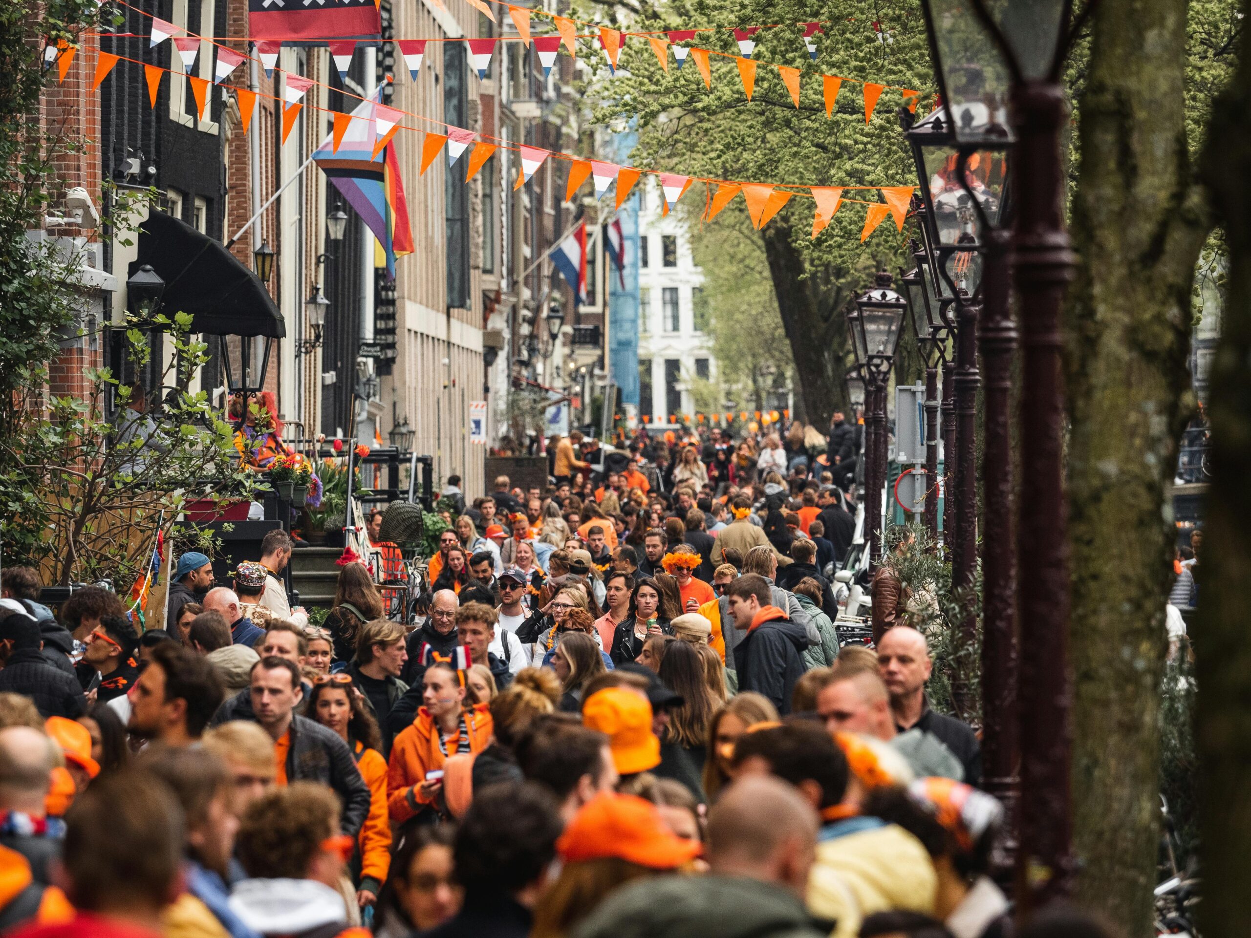Calle de los Países Bajos decorada con banderas naranjas y neerlandesas durante una celebración, con numerosas personas vestidas de naranja.
