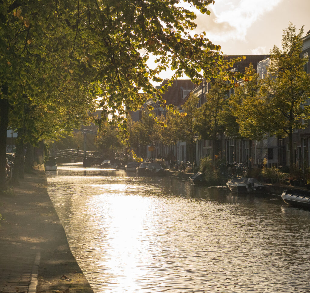 Canal de Leiden en un día soleado, con el reflejo del sol sobre el agua y edificios históricos a ambos lados.
