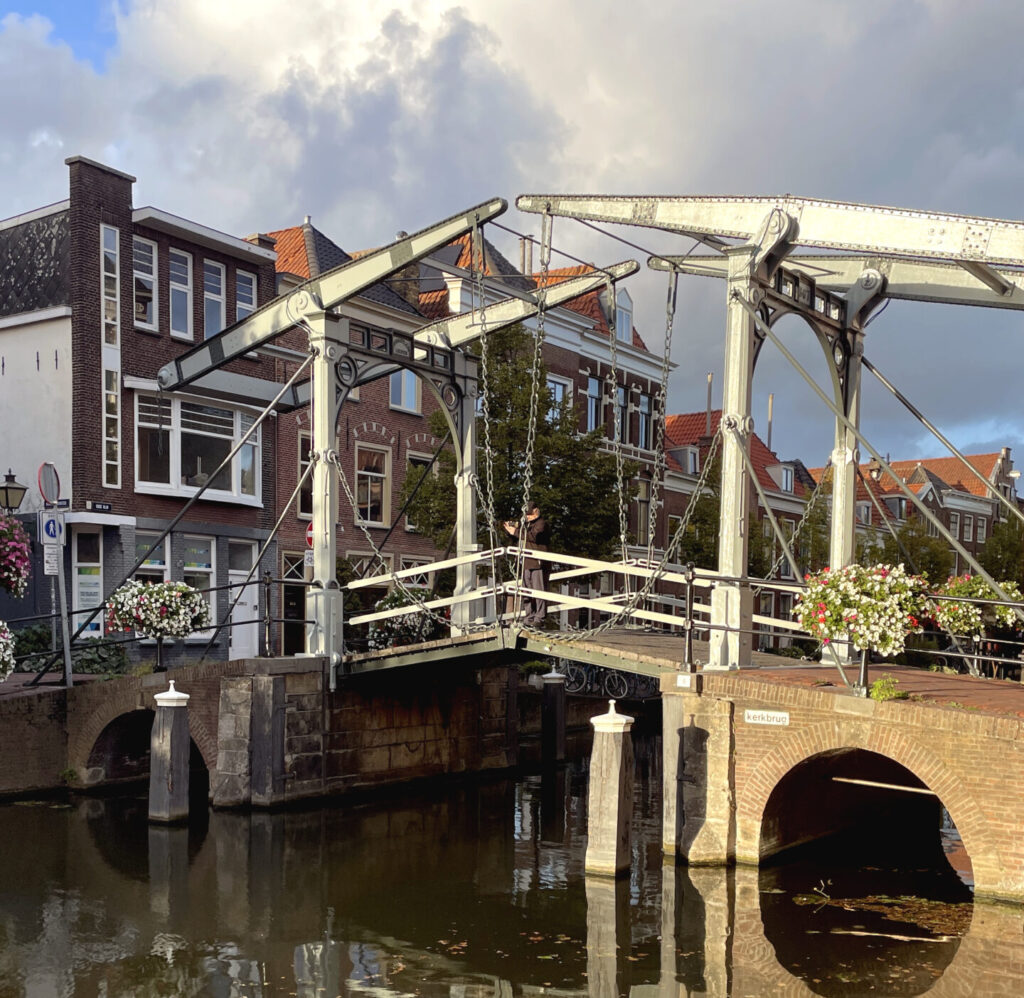 Puente levadizo sobre un canal de Leiden en un día soleado, con bicicletas y edificios históricos al fondo.