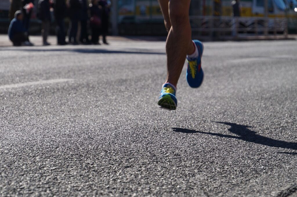 Primer plano de las piernas de un corredor avanzando solo por la carretera durante una prueba de atletismo.